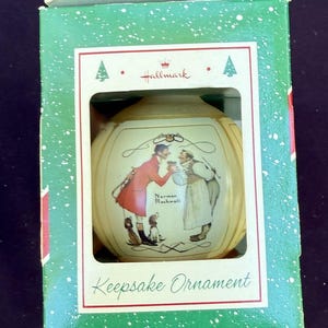 May include: A Hallmark Keepsake Ornament in a green and white box. The ornament features a painting by Norman Rockwell of two men and two dogs. The box reads "Keepsake Ornament".