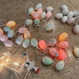 Puede incluir: Una cadena de luces en forma de huevo blancas, rosas y naranjas con un cable blanco. Las luces están enhebradas y listas para colgar como decoración.