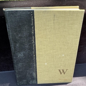 May include: A vintage book with a green and tan cover. The spine is dark green, and the front cover is tan with a large "W" and the text "Nineteen Sixty Seven Wesleyan College - Macon, Georgia".