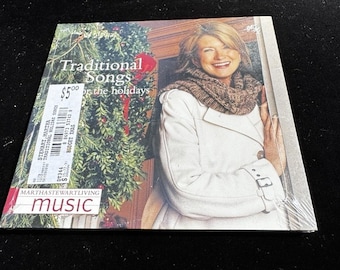 Könnte beinhalten: Eine CD mit dem Titel "Traditional Songs for the Holidays" mit einer Frau in einem weißen Mantel und Schal. Das Cover zeigt einen Weihnachtsbaum und den Text "Martha Stewart Living Music".