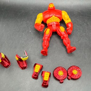May include: A red and yellow Iron Man action figure with detachable armor pieces. The figure is standing, with various armor components scattered around, including shoulder pads, leg pieces, and chest plates. The figure's design is based on the Marvel Comics character.