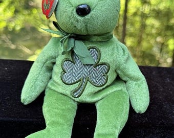 Peut inclure: Ours en peluche vert de la marque Beanie Baby avec un trèfle vert sur la poitrine. Le trèfle est fait d'un tissu gris et vert à motif tweed. L'ours a une étiquette rouge en forme de cœur attachée à son oreille gauche.