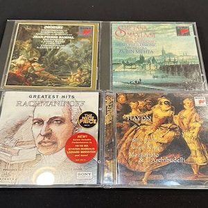 May include: Four compact discs in jewel cases featuring classical music composers. The top row features Mozart and Smetana. The bottom row features Rachmaninoff and Haydn. The Rachmaninoff disc has a red sticker that says "The Nice Price".