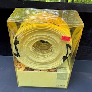 May include: A rolled-up yellow paper lantern with black accents, packaged in a clear plastic box. The lantern is cylindrical with multiple circular layers. The box has a Home O logo and a price tag.