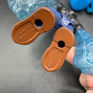 May include: Close-up of the feet of a blue action figure with brown soles. The soles are stamped with "&copy; 1996 MARVEL TOY BIZ, INC." and "MADE IN CHINA". The figure has blue and clear plastic ice-like attachments.