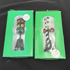 May include: Two miniature model railroad accessories in green boxes. One is a traffic light with red, yellow, and green lights. The other is a railroad crossing signal with red lights and a black and white striped pole.