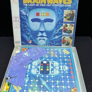 May include: A vintage board game called Brainwaves, The Light-Up, Fake-Out Strategy Game. The box features a blue face with a light-up feature. The game is for ages 8 to adult.