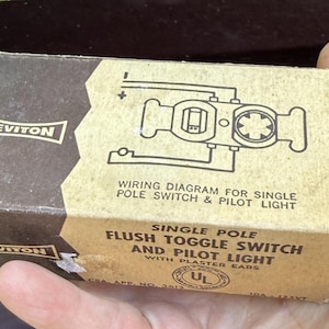 May include: Vintage Leviton electrical box. The box is tan and brown with the Leviton logo and text that reads "Wiring Diagram for Single Pole Switch & Pilot Light". The box also says "Single Pole Flush Toggle Switch and Pilot Light".