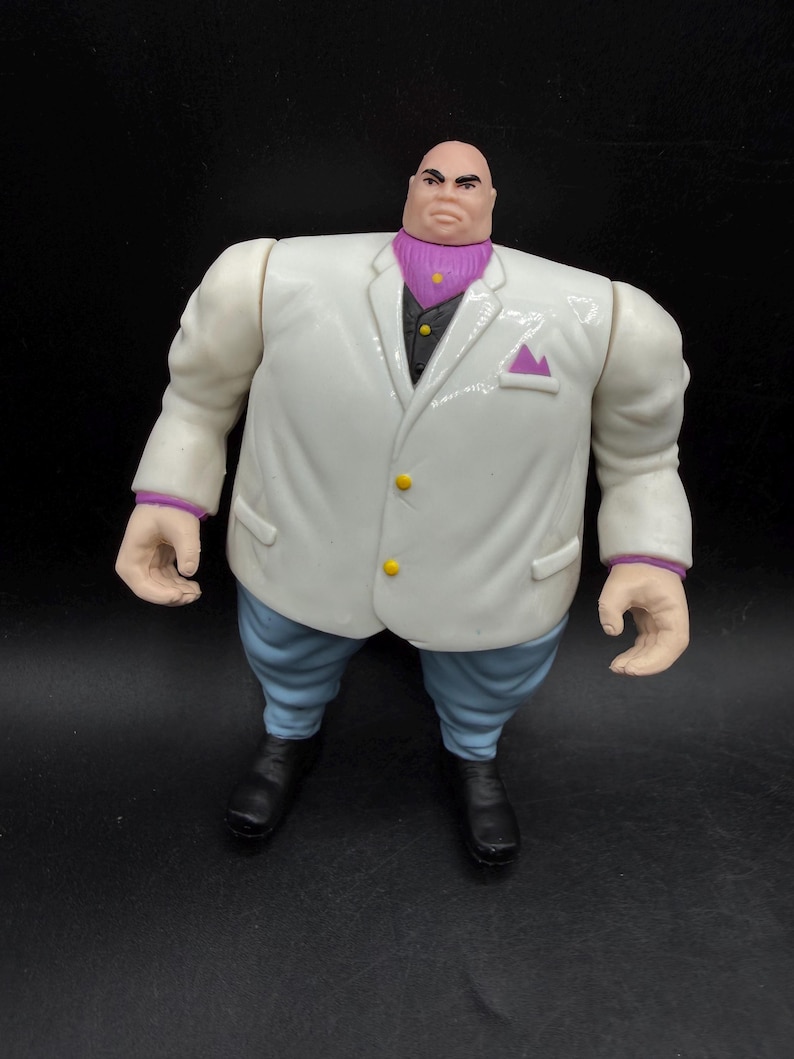 May include: A Kingpin action figure. The figure is wearing a white suit with a purple ascot and light blue pants. The figure has black shoes and a bald head. The suit has yellow buttons and a purple pocket square.