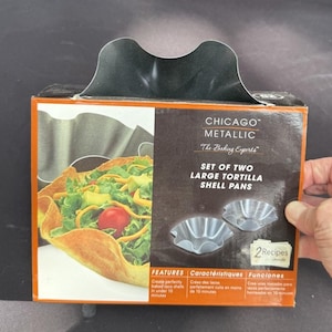 以下が含まれることがあります： Chicago Metallic の大きなトルティーヤシェルパン2個セット。箱には野菜が詰まったタコシェルの画像が掲載されています。箱には「The Baking Experts」と「2 Recipes inside」の文字も含まれています。