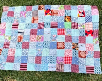 May include: A patchwork quilt with a blue background and squares of various colors and patterns, including red, pink, white, and green.