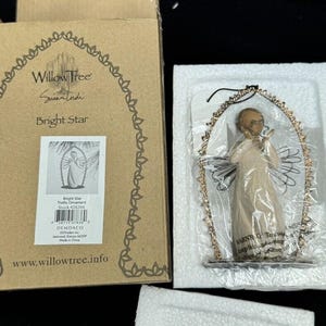 Könnte beinhalten: Ein Willow Tree Bright Star Ornament in der Originalverpackung. Die Engelsfigur befindet sich in einem goldfarbenen Rahmen. Die Schachtel ist braun und trägt die Aufschrift "Willow Tree" und "Bright Star".