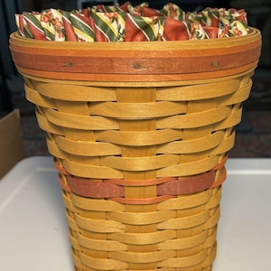May include: A woven wicker basket with a red and orange trim. The basket is lined with a fabric liner with a floral and striped pattern in shades of red, green, and yellow.