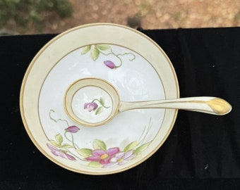 May include: A vintage porcelain serving set featuring a small bowl and a matching spoon. The set is decorated with pink and purple floral designs, green leaves, and gold trim. The bowl has a cream-colored border.