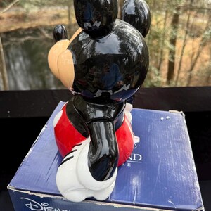 May include: A glossy black Mickey Mouse figurine with red shorts, white gloves, and tan ears. The figurine is on top of a blue Disney box. The figurine is a collectible item.