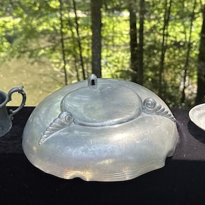 May include: A set of three vintage pewter pieces, including a small cup with a floral design, a lidded bowl with a decorative swirl design, and a small dish with a pedestal.