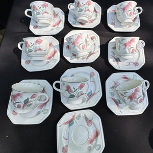 Puede incluir: Juego de diez tazas de té y platillos blancos con diseños florales en tonos rosa, verde y marrón. Las tazas y los platillos tienen una forma cuadrada con esquinas redondeadas.