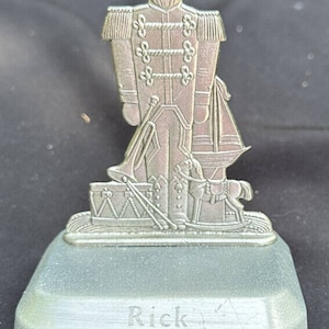 Puede incluir: Porta calcetines de Navidad plateado con una figura de cascanueces con un tambor y un caballo de balancín. El soporte tiene una base con el nombre "Rick" grabado en él.