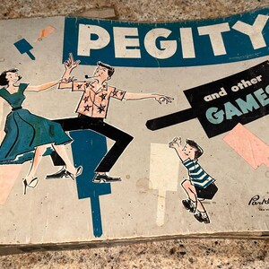 Peut inclure: Boîte de jeu vintage avec une illustration bleue et blanche de personnes jouant à des jeux. La boîte est intitulée "Pegity et autres jeux" et porte la date de copyright 1948.