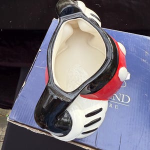 May include: A ceramic Mickey Mouse-shaped container. The container is primarily white, with a red body and black accents. The interior is white. The container is sitting on a blue box.