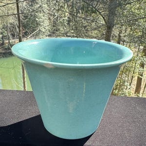 May include: A light blue ceramic planter with a wide, rounded rim. The planter is smooth and has a slightly textured surface.
