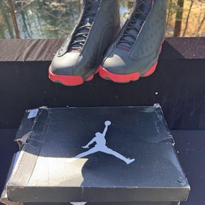 May include: Pair of black and red high-top sneakers with a matching black box featuring a white silhouette of a basketball player. The sneakers have red soles and accents, and black laces.