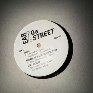 Puede incluir: Un disco de vinilo blanco con texto negro. El disco se titula "Ear 2 Da Street" y presenta una lista de canciones con artistas como Amerie, Birdman, Lil Wayne, Rick Ross, T Pain y Janet Jackson. El número del disco es E2DS-155.
