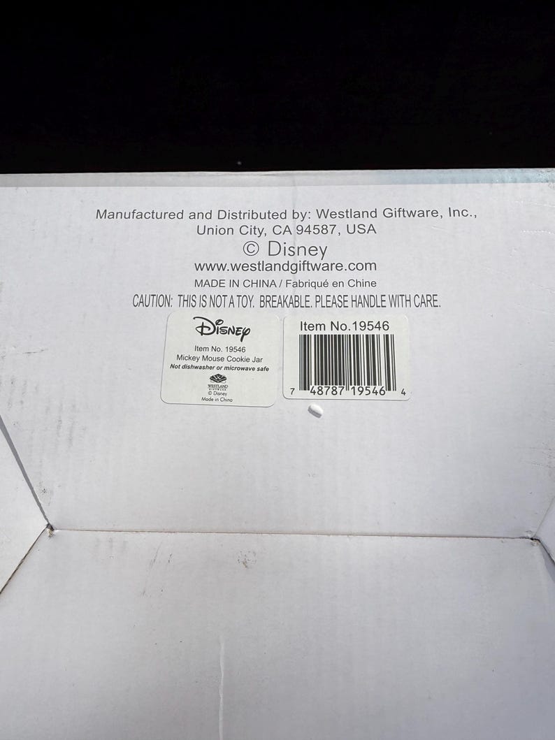 May include: White cardboard box with text including "Disney" and "Mickey Mouse Cookie Jar." The box also has a barcode and the text "CAUTION: THIS IS NOT A TOY. BREAKABLE. PLEASE HANDLE WITH CARE."