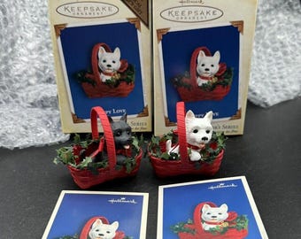 Può includere: Due ornamenti Hallmark Keepsake con un cucciolo bianco e un cucciolo nero in cesti rossi con agrifoglio verde. Gli ornamenti sono confezionati in scatole blu con una corona dorata e il testo "Hallmark Keepsake Ornament". Gli ornamenti hanno anche un'etichetta con il testo "Puppy Love".