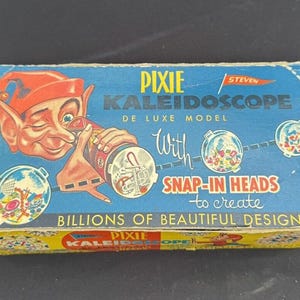 Könnte beinhalten: Eine Vintage-Verpackung für ein Pixie Kaleidoscope De Luxe Model mit einer bunten Illustration eines Kobolds, der ein Kaleidoskop hält. Auf der Verpackung steht "With Snap-In Heads to create Billions of Beautiful Designs".