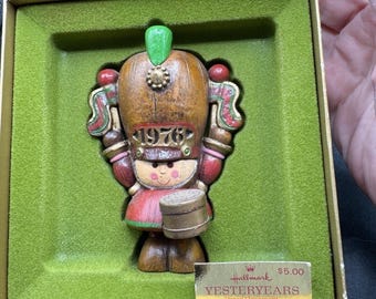 Könnte beinhalten: Ein Vintage-Weihnachtsornament von Hallmark aus dem Jahr 1976 mit der Aufschrift "Yesterday Years", das eine Trommlerin in einem rot-goldenen Uniform mit einem grünen Hut zeigt. Das Ornament befindet sich in seiner Originalverpackung mit einem Preisschild, auf dem "5,00 $ " steht.
