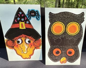 May include: Two vintage Halloween decorations. One is a witch's face with a black hat, orange hair, and a long nose. The other is a black owl with large orange eyes. A blue spider is attached to the witch's hat.
