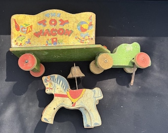 Könnte beinhalten: Ein antiker Holzspielzeugwagen mit grün-gelb bemaltem Korpus. Der Wagen wird von einem rot-weiß bemalten Pferd gezogen. Der Wagen hat eine Glocke oben und die Worte "The Toy Wagon" sind an der Seite bemalt.