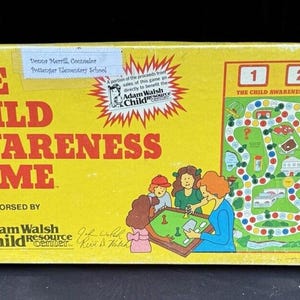Może przedstawiać: Żółte pudełko gry planszowej z tytułem "THE CHILD AWARENESS GAME" w czerwonych literach. Pudełko zawiera ilustracje dzieci grających w grę i planszę. Adam Walsh Child Resource Center popiera grę.