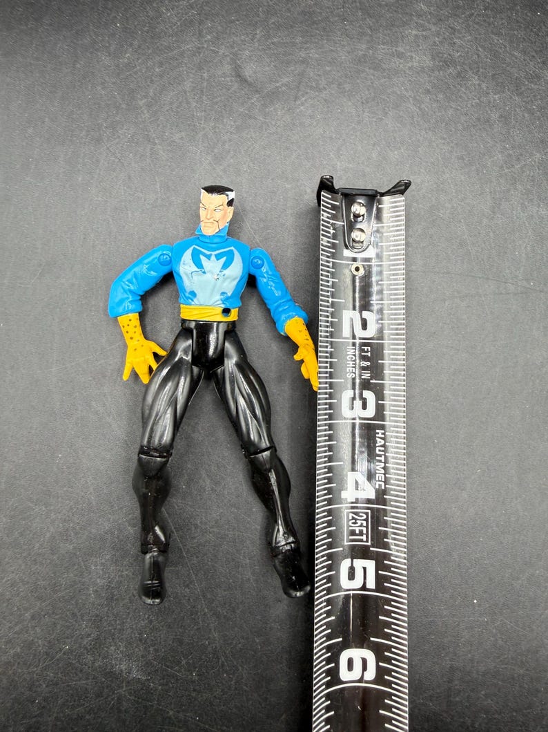May include: A plastic action figure of a character in a blue and yellow costume with black pants. The figure is approximately 5 inches tall. The figure is standing next to a measuring tape.