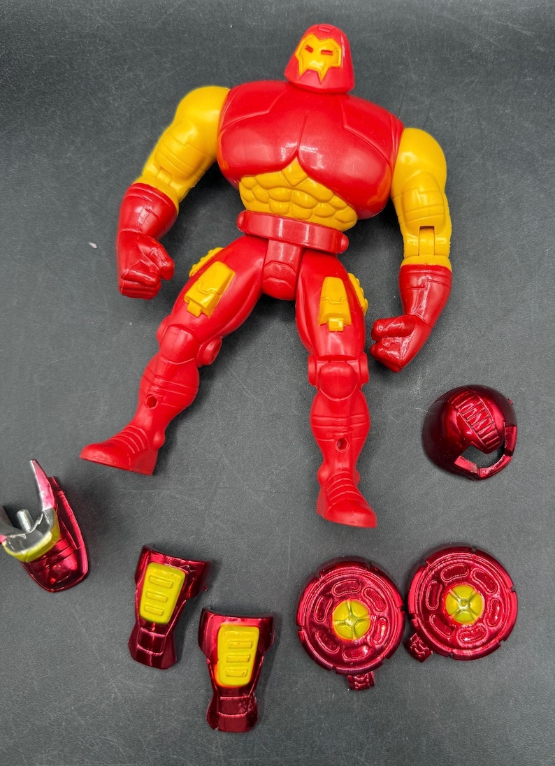 May include: A red and yellow action figure of a superhero, with detachable parts. The figure has a red helmet, chest, legs, and feet, with yellow arms and accents. Additional red and yellow pieces are scattered around the figure.