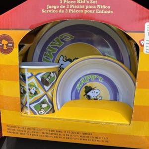May include: A Snoopy Happy Camper 3-piece kid's set in a yellow and red box. The set includes an 8-inch plate, a 5 1/2-inch bowl, and an 11 oz tumbler. Each piece features Snoopy in a camping theme with a yellow, purple, and white color scheme.