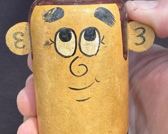 May include: A wooden birthday figurine with a smiling face, black shoes, and a sign that reads "STOP WHILE YOU'RE AHEAD HAPPY BIRTHDAY." The figurine has two round ear-like pieces with the numbers "3" and "ε" on them.