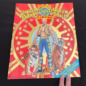 May include: A vintage Ringling Bros. and Barnum & Bailey Circus program cover. The cover features a man in a circus outfit with two tigers. The background is red with gold accents and text that reads "The Greatest Show on Earth".