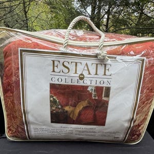 May include: A red and gold Estate Collection comforter set in a clear plastic zippered bag with a rope handle. The label reads "Estate Collection" with a picture of the comforter set. The comforter set is oversized and overfilled.