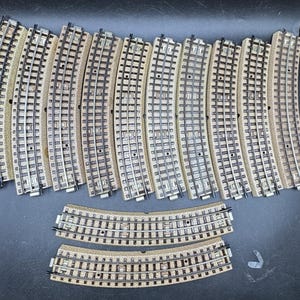 May include: A collection of model train tracks, including curved and straight sections. The tracks are made of a light brown material with silver-colored rails. The tracks are arranged on a dark surface.