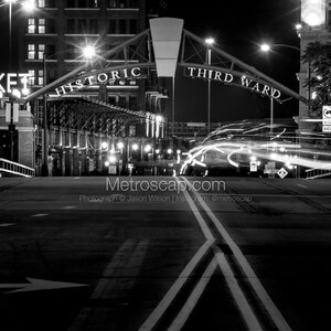 Könnte beinhalten: Ein Schwarzweißfoto einer Straße bei Nacht mit einem Schild, auf dem "Historic Third Ward" steht, über der Straße. Die Straße ist leer, bis auf ein paar Autos in der Ferne. Die Straße ist an beiden Seiten von Gebäuden gesäumt.