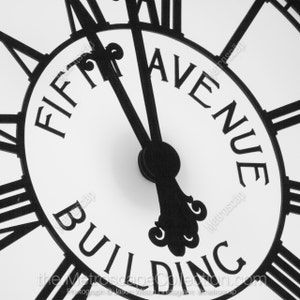 Puede incluir: Cara de reloj en blanco y negro con números romanos y las palabras "Fifth Avenue Building" en la cara.