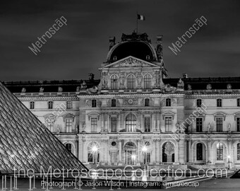 Puede incluir: Una fotografía en blanco y negro del Museo del Louvre en París, Francia, de noche. La icónica pirámide de vidrio está en primer plano, con la fachada del Louvre visible en el fondo.