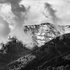 May include: A black and white photograph of a mountain range with snow-capped peaks and clouds in the sky.