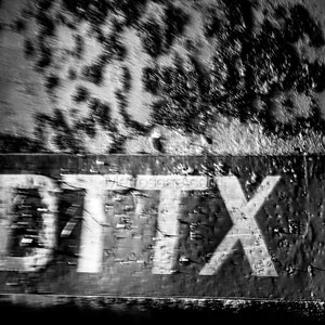 Puede incluir: Una foto en blanco y negro de una superficie metálica desgastada con el texto "DTX7" pintado en blanco.