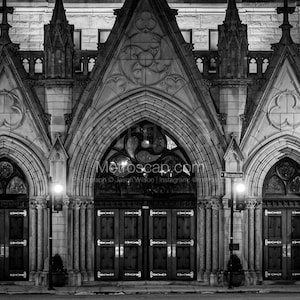 May include: Black and white photo of a church entrance with two large wooden doors. The doors are arched and have decorative ironwork. The church is made of stone and has a gothic style architecture.