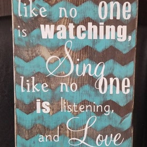 May include: Wooden sign with a turquoise and brown chevron pattern. The sign has white text that reads "Dance like no one is watching, Sing like no one is listening, and Love like you have never been hurt."
