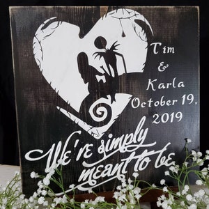 May include: Black wooden sign with white painted silhouettes of Jack Skellington and Sally from the Nightmare Before Christmas movie. The sign reads "Tim & Karla October 19, 2019 We're simply meant to be".