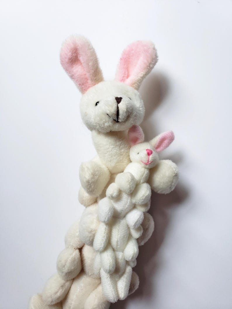May include: A stack of white plush bunny toys with pink ears. The top bunny is the largest and has a smaller bunny nestled in its arms.